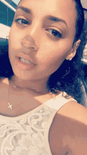 a woman wearing a white tank top and a cross necklace takes a selfie