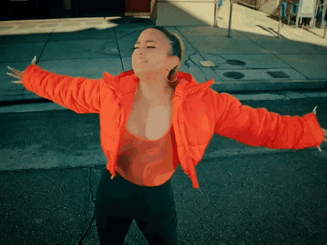 a woman with her arms outstretched is wearing an orange jacket