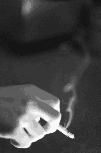 a black and white photo of a person holding a cigarette with smoke coming out of it
