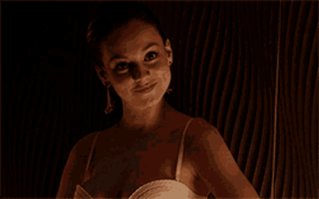 a woman wearing a white bra and earrings is standing in a dark room