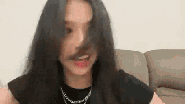 a woman is sitting on a couch with her hair blowing in the wind and making a funny face .