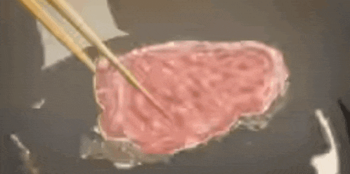 a piece of meat is being cooked with chopsticks in a pan .