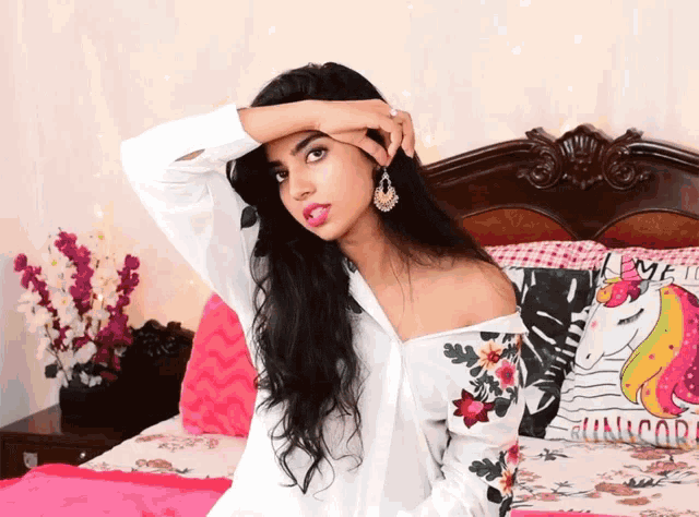 a woman sitting on a bed with a pillow that says unicorn on it