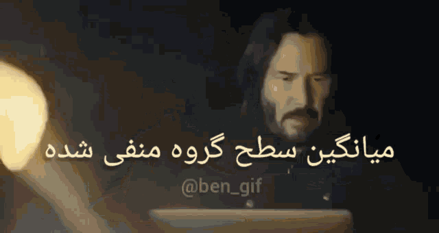 a man with a beard is sitting in front of a laptop with a foreign language behind him