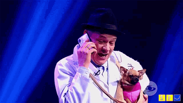 a man talking on a cell phone while holding a dog
