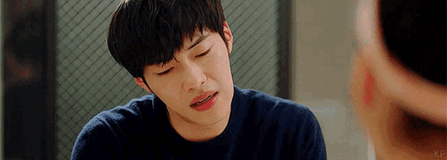a young man is sitting at a table with his eyes closed and looking at another man .