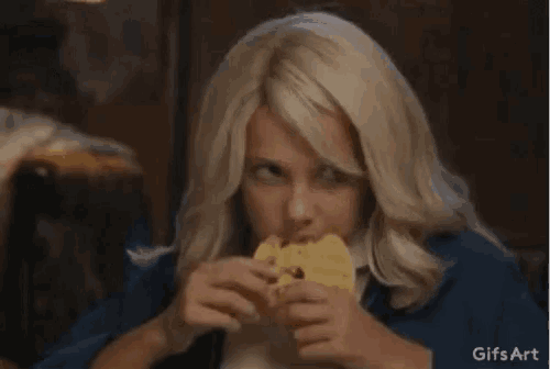 a woman is sitting at a table eating a hamburger .