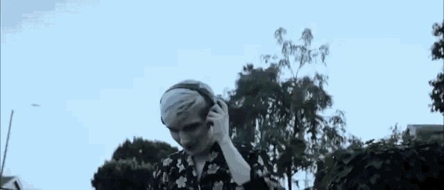 a man with white paint on his face is wearing headphones and standing in front of trees .