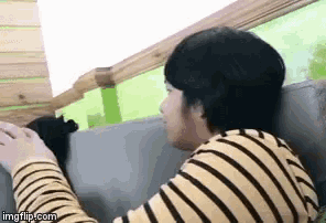 a man in a yellow and black striped shirt is petting a black cat