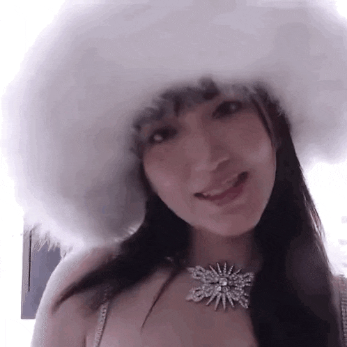 a woman wearing a white fur hat and a necklace is smiling at the camera .