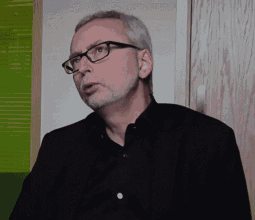 a man wearing glasses and a black shirt looks to his left