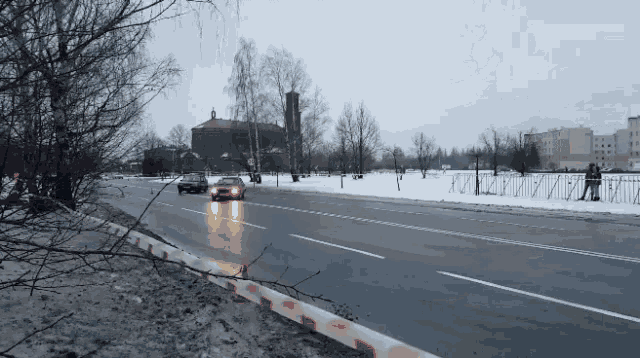 a car is driving down a snowy road with a fence in the foreground