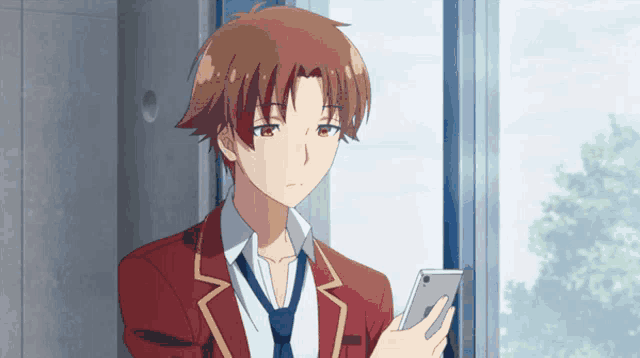 a young man in a red suit and tie is looking at his phone