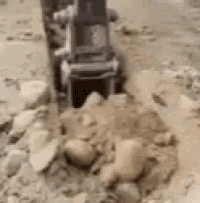 a tractor is driving through a pile of rocks in the dirt .