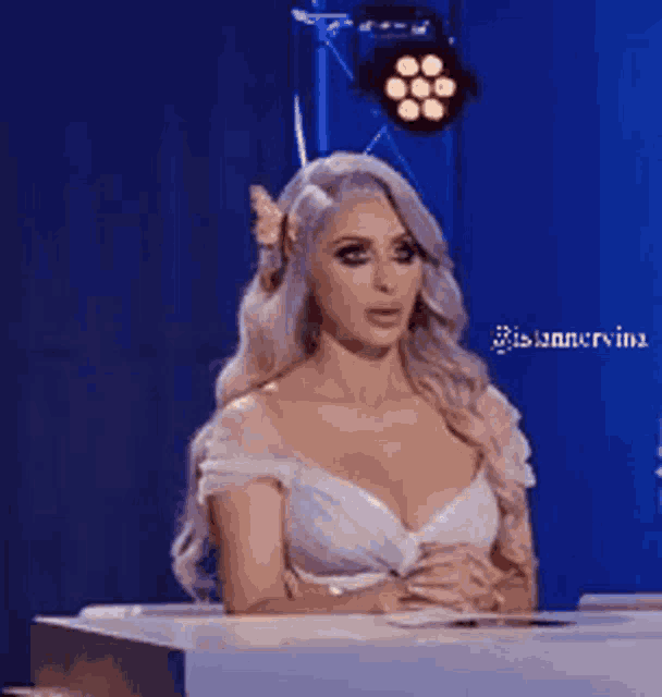 a woman in a white dress is sitting at a table with a blue background .