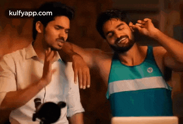 two men are standing next to each other and one of them is putting ear buds in his ears .
