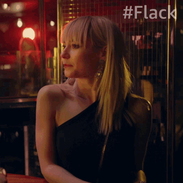 a woman in a black dress sits at a table in front of a sign that says #fleck