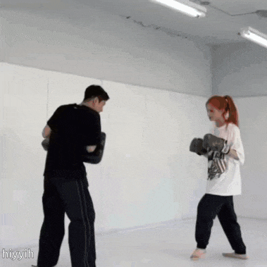 a man and a woman are boxing in a gym and the woman is wearing a white shirt that says hiyyil