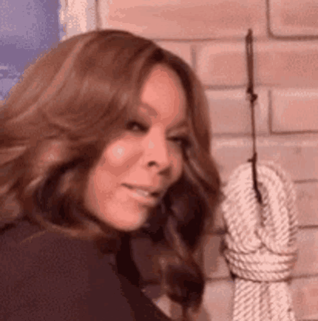 a woman is smiling while standing next to a rope hanging on a brick wall .