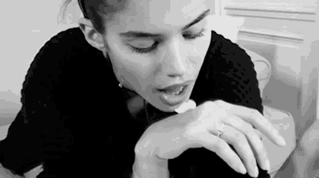 a black and white photo of a woman sitting on a couch with her eyes closed and a ring on her finger .