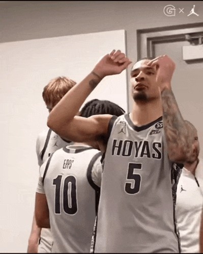 a basketball player wearing a hoyas 5 jersey stands in a locker room