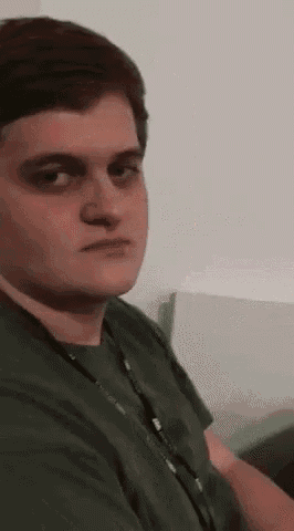 a young man in a green shirt is sitting on a couch looking at the camera .