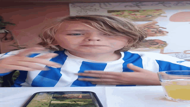 a young boy wearing a blue and white striped shirt sitting at a table