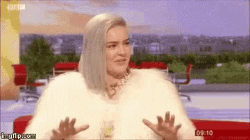 a woman is sitting on a couch wearing a fur coat and making a funny face .