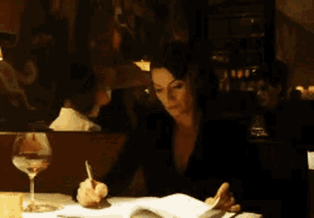 a woman is writing on a piece of paper with a pen while a man stands behind her .