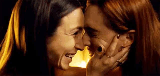 a couple of women are touching each other 's faces and smiling .