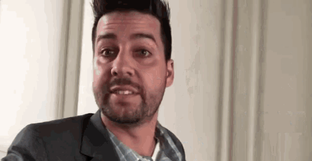 a man with a beard is wearing a suit and a plaid shirt .