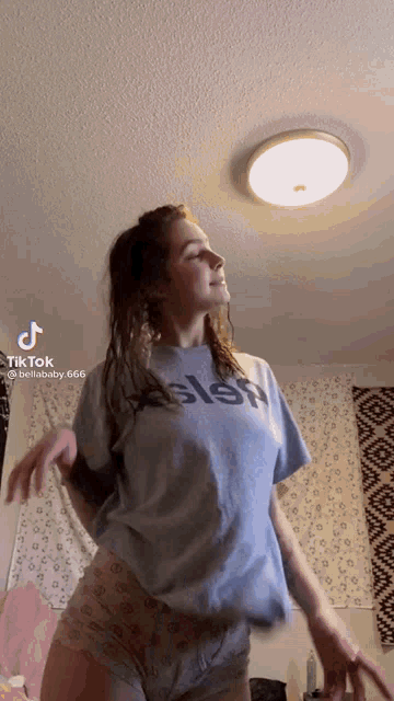 a woman in a blue t-shirt is dancing in a room with a light on the ceiling ..