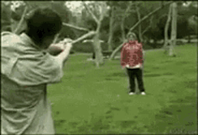 a man is pointing a gun at a woman in a red jacket in a park