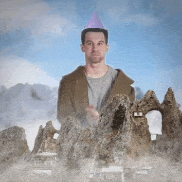 a man wearing a purple party hat stands in front of a mountain