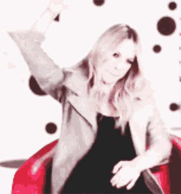 a woman in a black dress is sitting in a red chair with her arm in the air