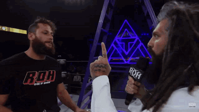 a man in a roh shirt is talking to another man with dreadlocks