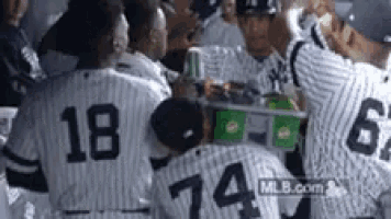 a group of baseball players are sitting around a table with a cooler in the middle .
