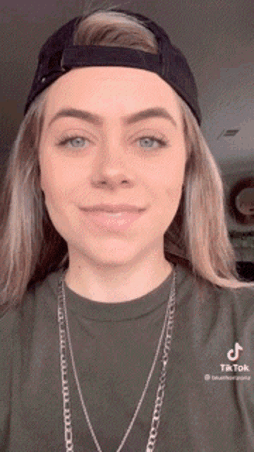 a woman wearing a baseball cap and a necklace is smiling for the camera .