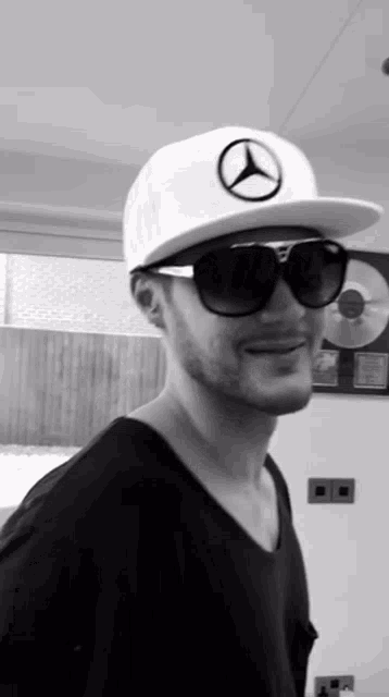a man wearing sunglasses and a white mercedes hat
