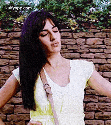 a woman in a yellow dress is standing in front of a brick wall with her hands on her hips .