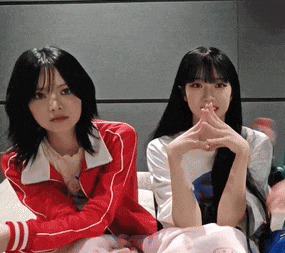 two young women are sitting next to each other with their hands folded