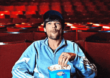 a man in a blue jacket is eating popcorn from a blue bucket that says waffle 's on it