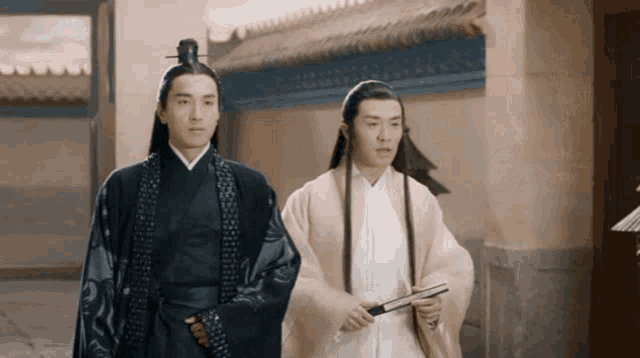 two men with long hair are standing next to each other in front of a building