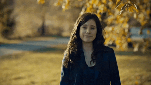 a woman in a black coat is standing in a field