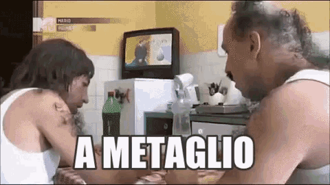 two men are sitting at a table in front of a television and the words a metaglio are written on the screen