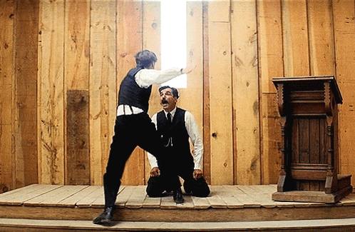 two men are kneeling on a stage with a wooden wall in the background