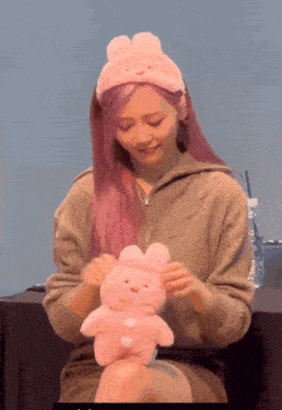 a woman with pink hair is holding a pink teddy bear