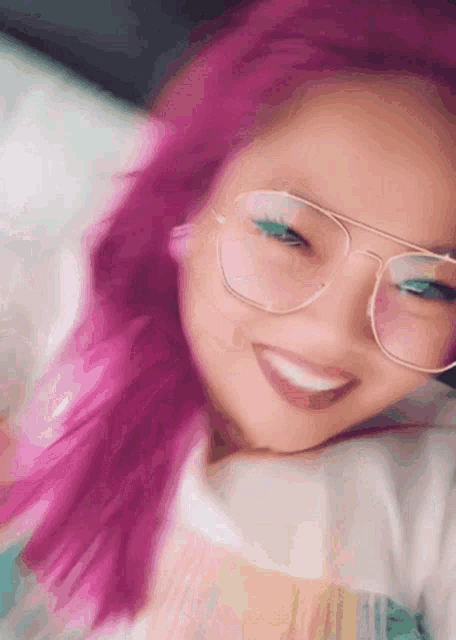 a girl with pink hair wearing glasses and smiling