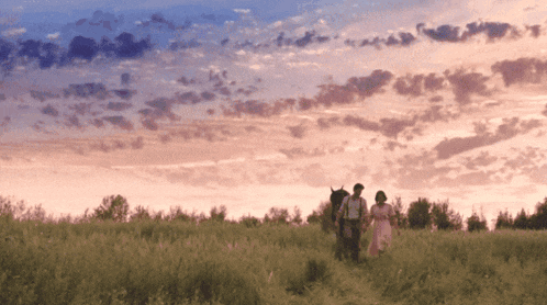 a man and a woman walking in a field with a pink sky in the background