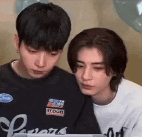 a couple of young men are sitting next to each other and looking at a laptop .